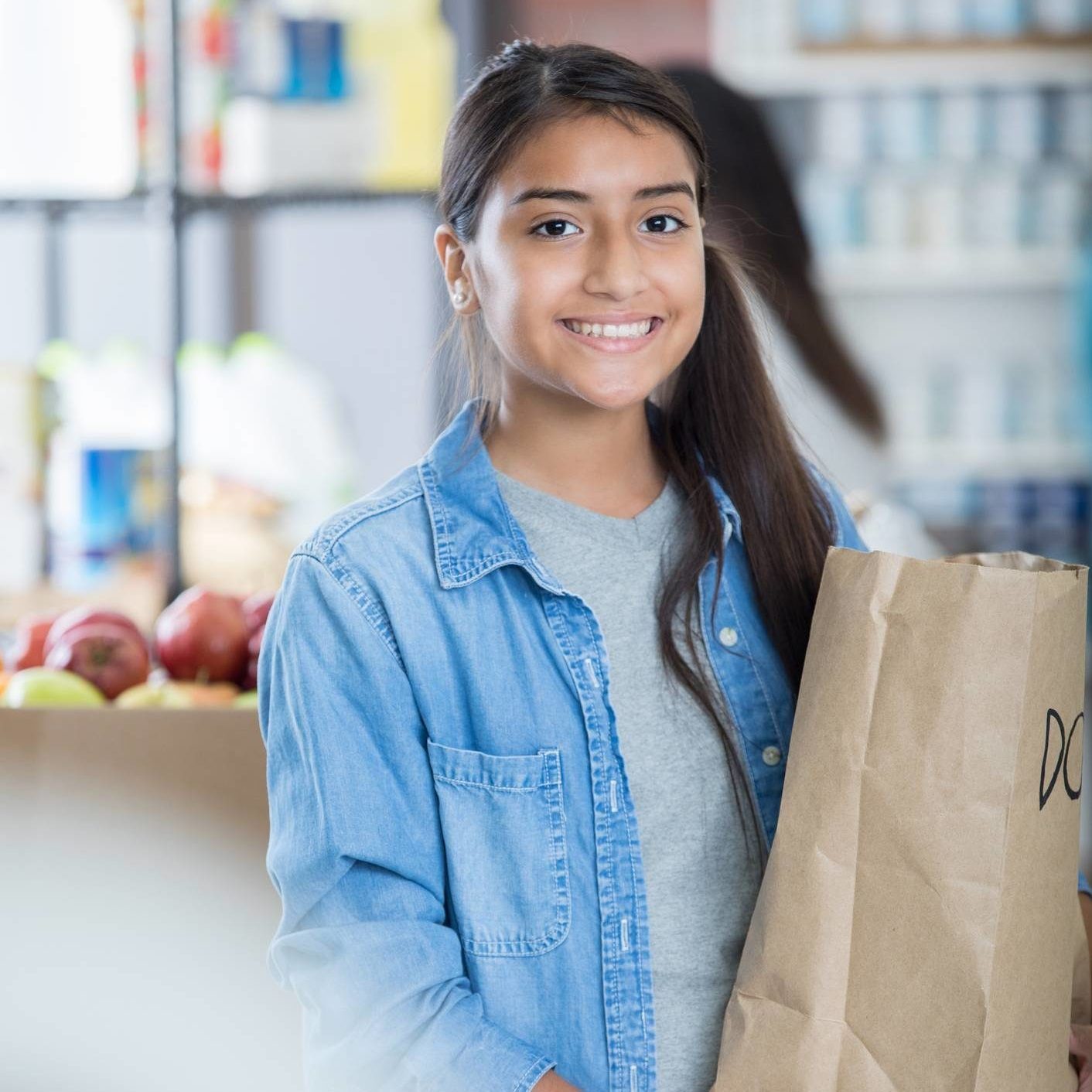 Pretty preteen girl holds a bag of donated groceries. She is volunteering in a community food bank.